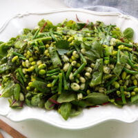 a platter with herby green bean salad served on a bed of lettuce