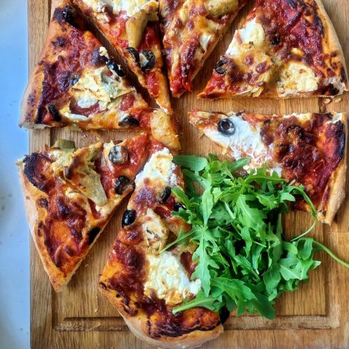 vegetarian pizza with homemade rich tomato sauce on a serving board garnished with rocket
