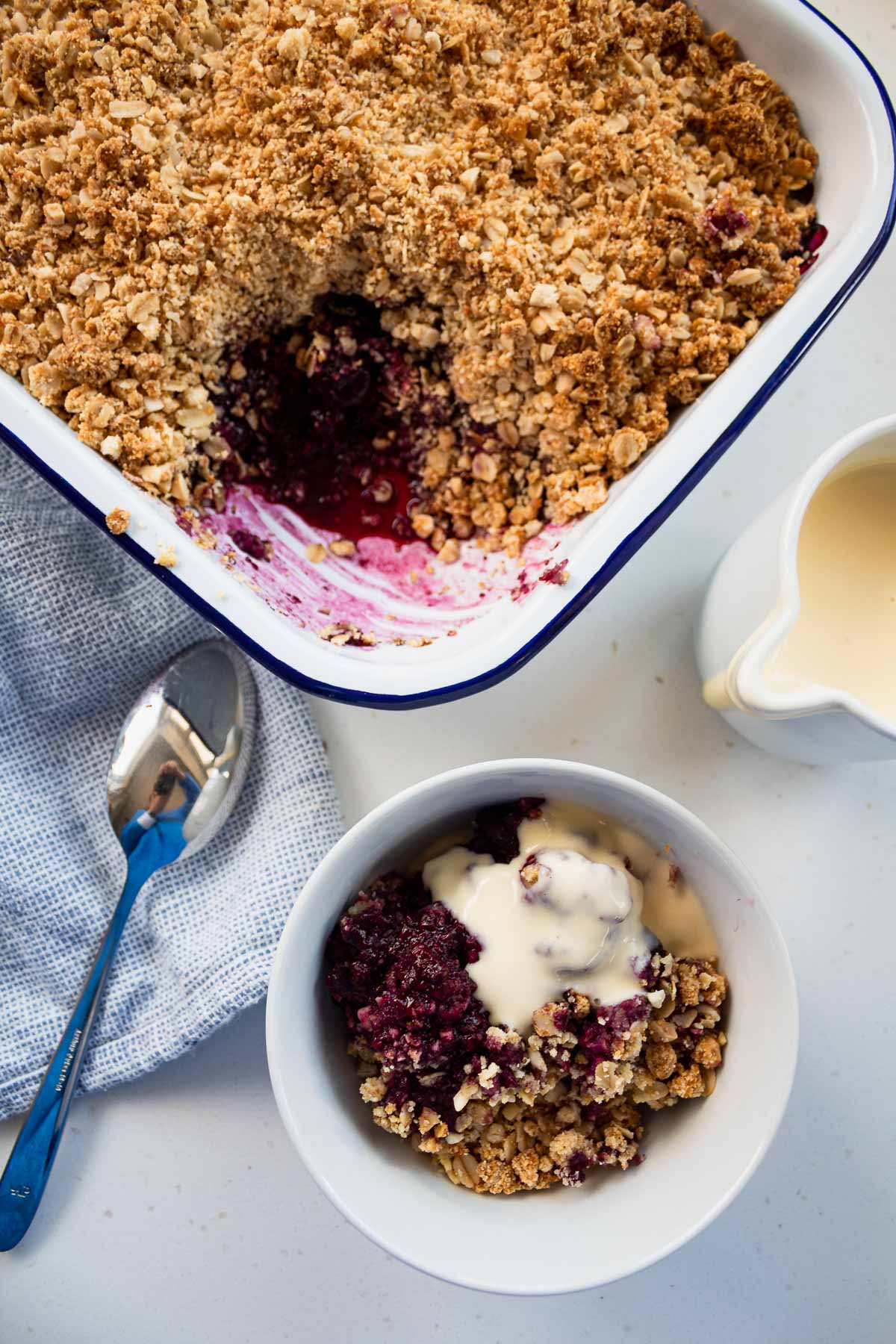 healthy berry crumble served from the oven dish in a bowl with a jug of custard