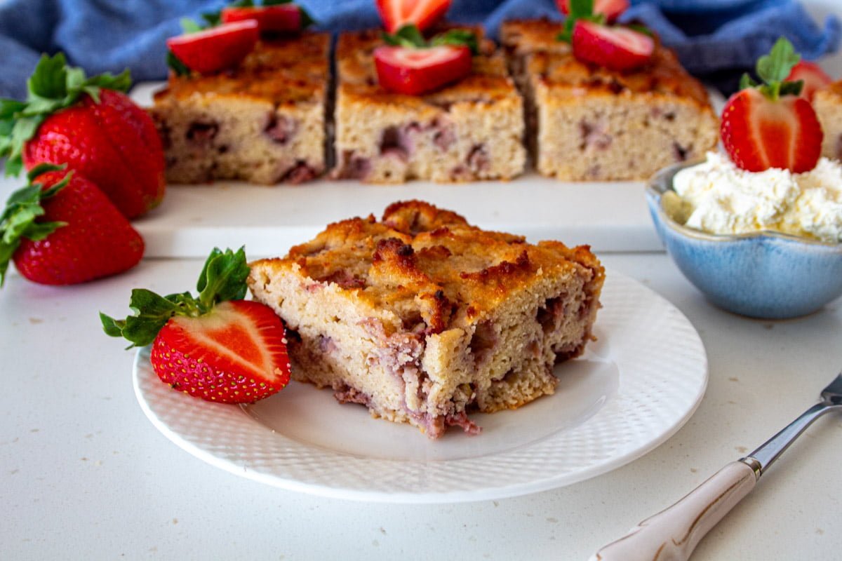 square piece of sugar free strawberry cake on a plate with cake in the background