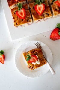 piece of sugar free strawberry cake on a plate and the cake in the background with fresh strawberries