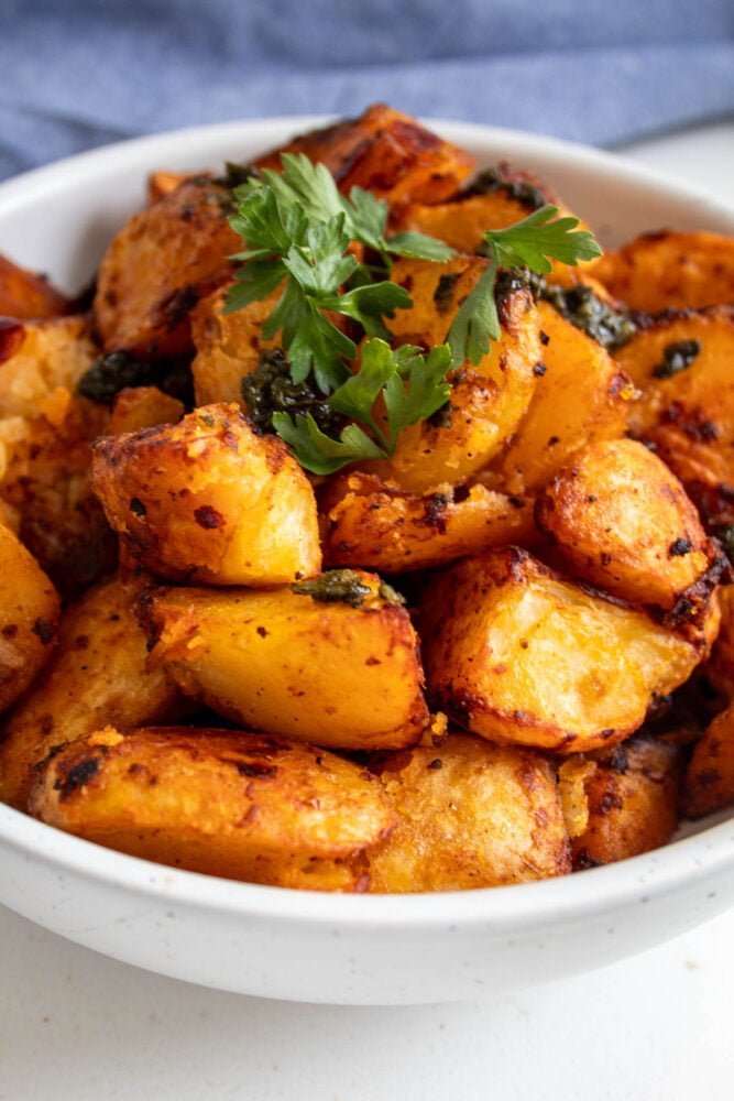 harissa roasted potatoes piled up in a bowl with parsley and chopped herbs