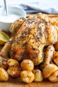 Greek style Roast Chicken with Roast Potatoes on a board with lemon and yoghurt dip
