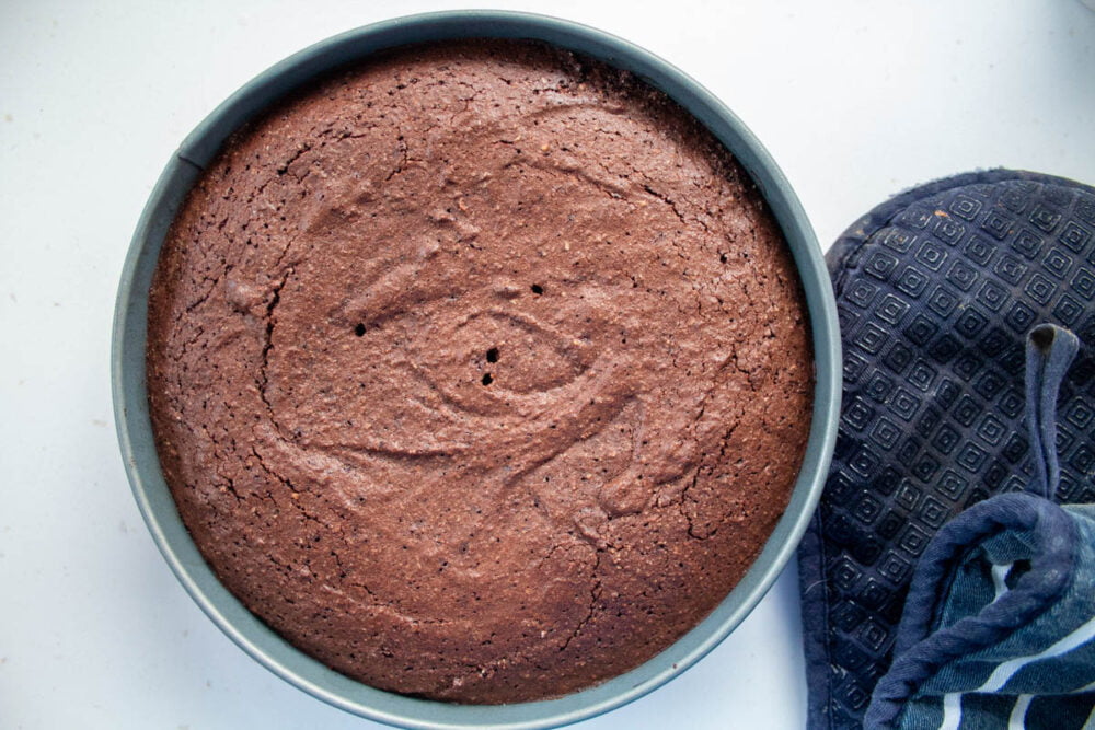 cooked chocolate torte in a spring form pan with oven gloves at the side