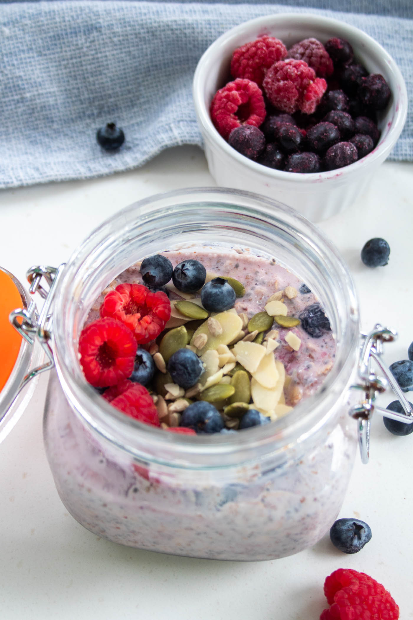 overnight oats with frozen berries in a mason jar topped with nuts, seeds and fresh berries