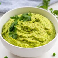 vibrant green pea hummus in a bowl with parsley garnish and peas