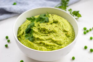 vibrant green pea hummus in a bowl with parsley garnish and peas