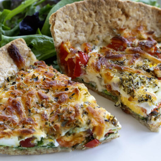 A closeup of a two slices of breakfast tortilla pizza on a white plate with salad leaves