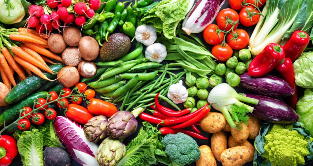A selection of brightly coloured vegetables laid out from green beans, radishes, garlic lettuce to peppers and artichokes