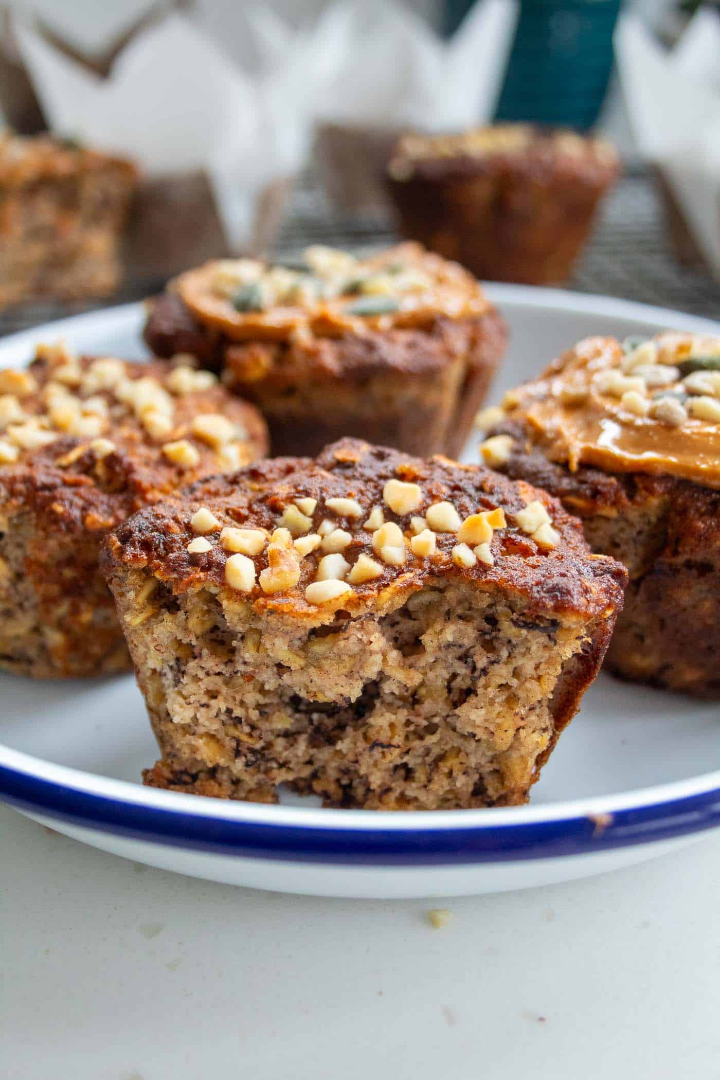 a closeup of half a banana oat muffins in a white dish with blue rim with chopped nuts on top and more muffins visible in the background.
