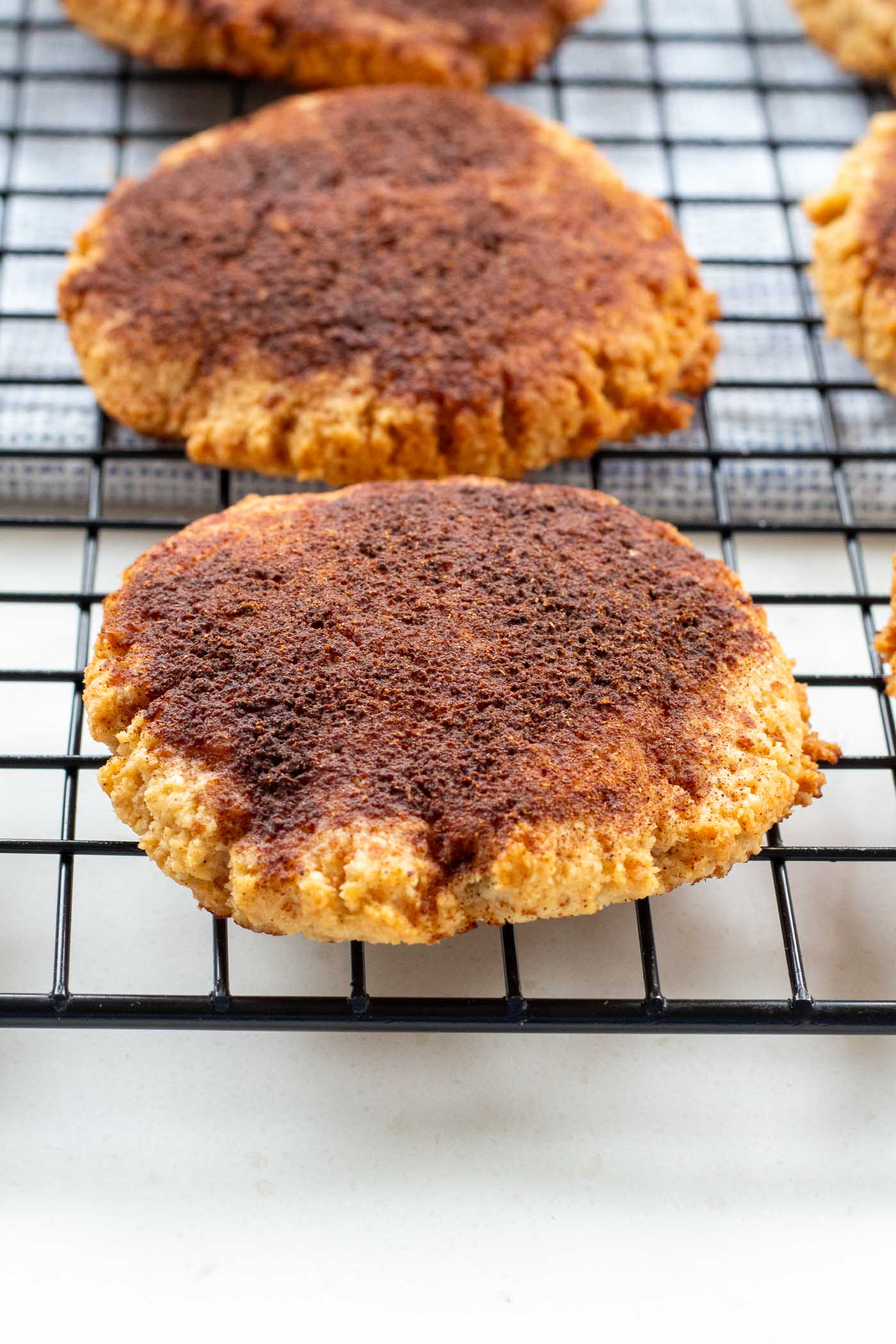 Close-up of a healthy cinnamon cookie on a cooling rack showing their golden-brown texture and cinnamon dusting.
