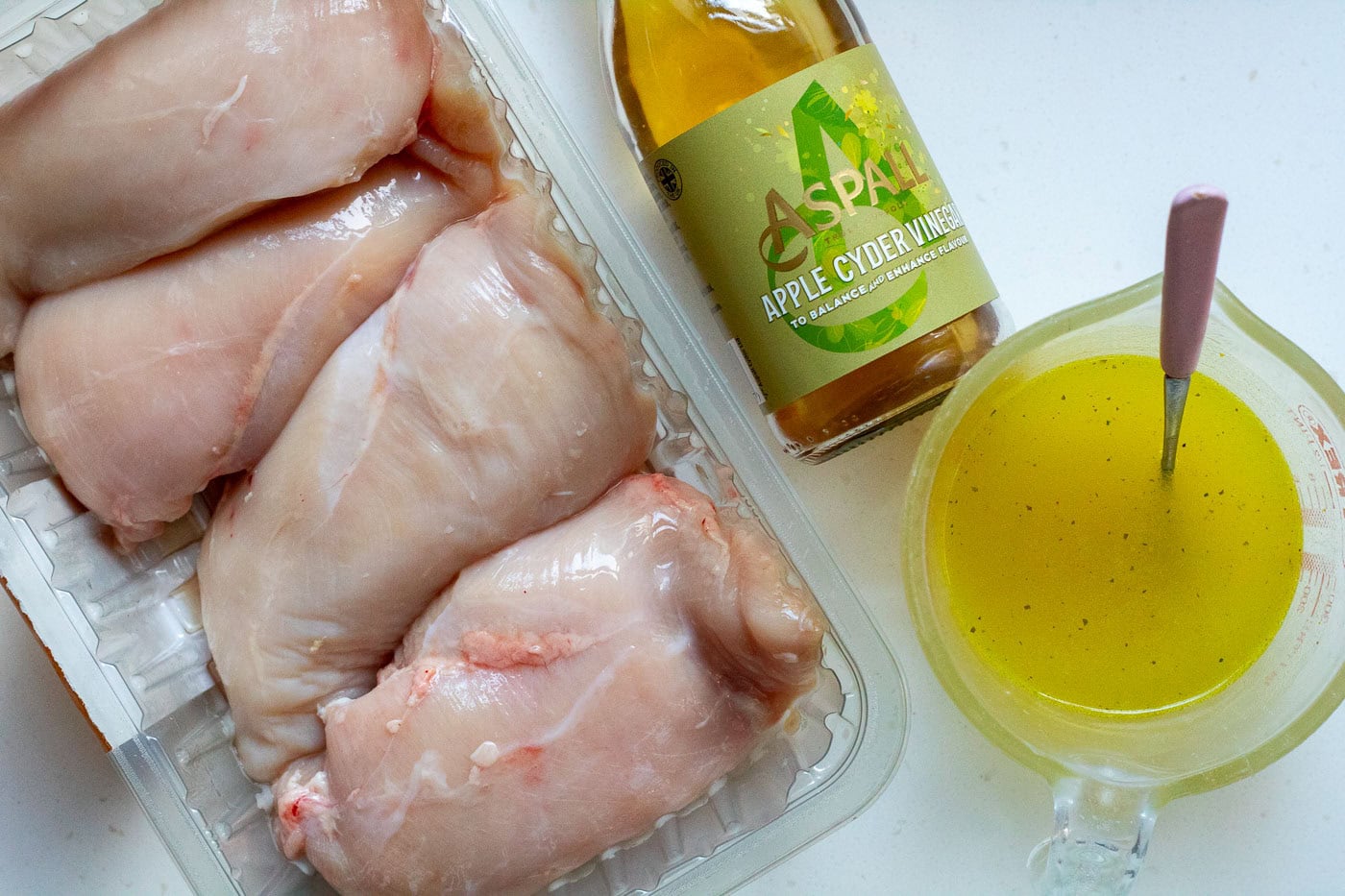 Ingredients for crockpot shredded chicken from chicken breasts, chicken stock and apple cider vinegar laid out on a white background