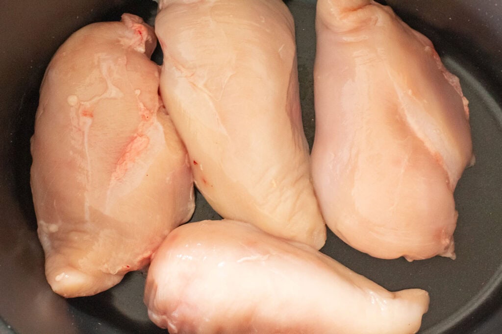 Raw chicken breasts placed in a slow cooker ready to cook for easy shredded chicken meal prep