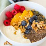 Balanced yoghurt bowl with granola, chia seeds, blueberries, raspberries, peach slices and walnuts, high fibre and protein breakfast idea