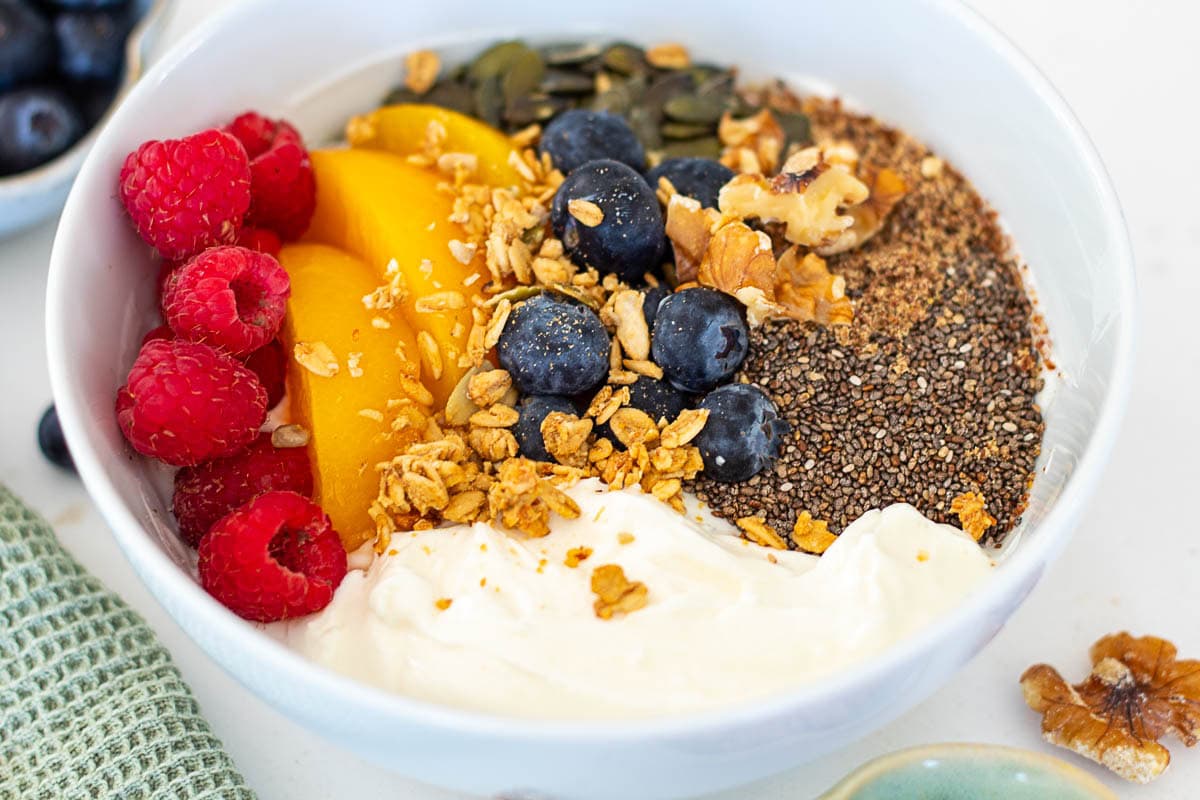 Balanced yoghurt bowl with granola, chia seeds, blueberries, raspberries, peach slices and walnuts, high fibre and protein breakfast idea
